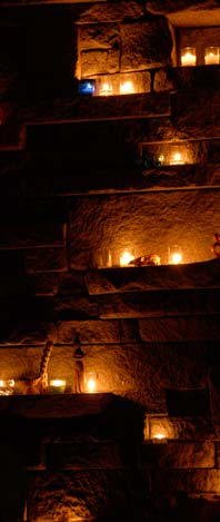 Picture of rock wall warmly lit with dozens of votive candles.